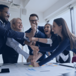 A quintet of remote staff colleagues working in the hospitality industry boosting each other's morale in the workplace, uniting their fists in an upward stack.